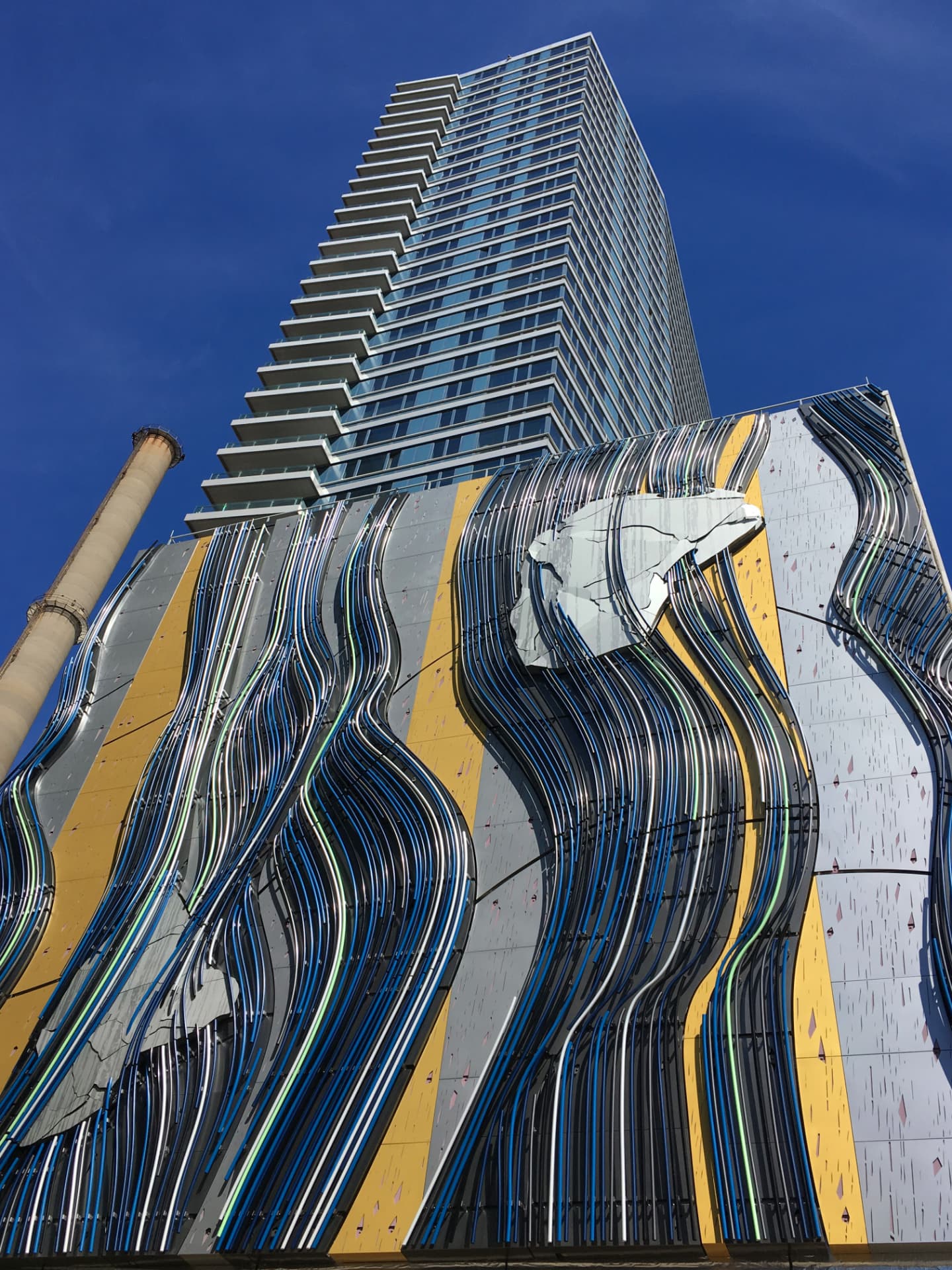 High-rise tower with a curved multicolor striped metal facade feature at street level