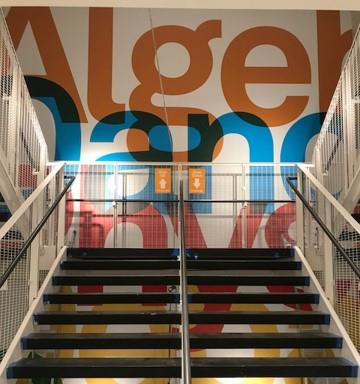 Oversized colorful typographic wall mural rising above an interior staircase.