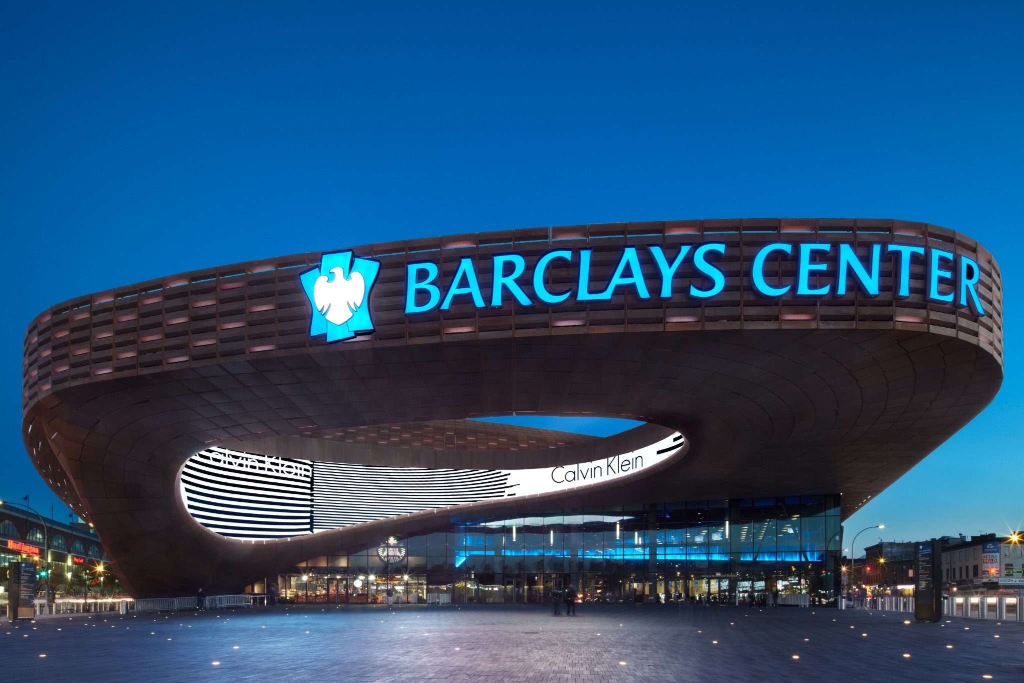 Barclays Center exterior at dusk with illuminated channel-letter identification on the weathered steel facade
