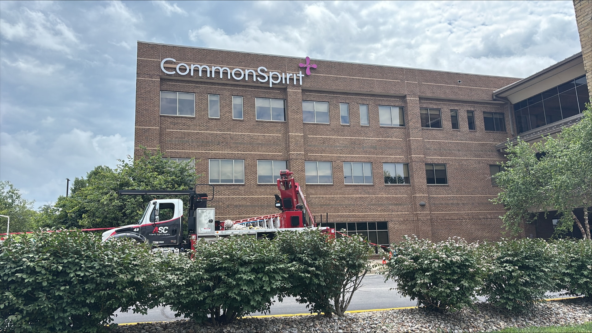 CommonSpirit building identification letters on a brick hospital facade with an AIS crane truck staged below