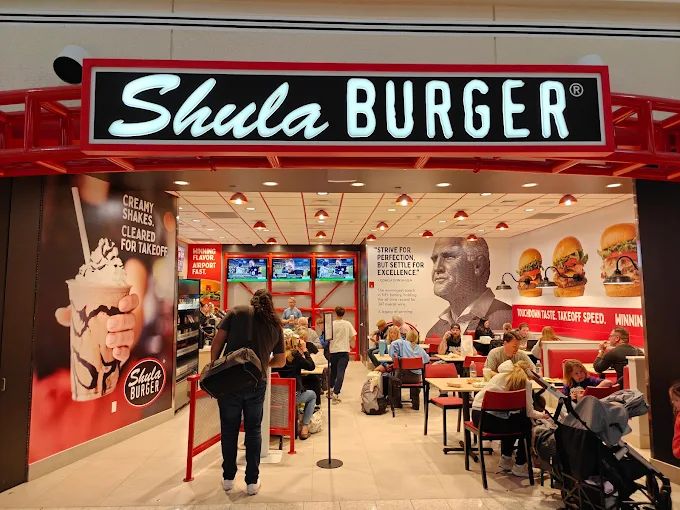 Shula Burger restaurant entry with an illuminated black and red channel-letter sign and interior wall graphics