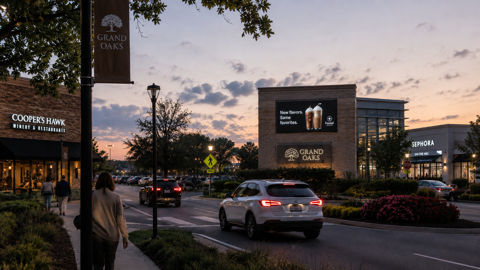 Outdoor LED display at a retail lifestyle center at dusk, showcasing a beverage campaign above the Grand Oaks sign.