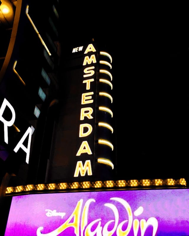 Illuminated New Amsterdam Theatre vertical blade sign and marquee on Broadway at night